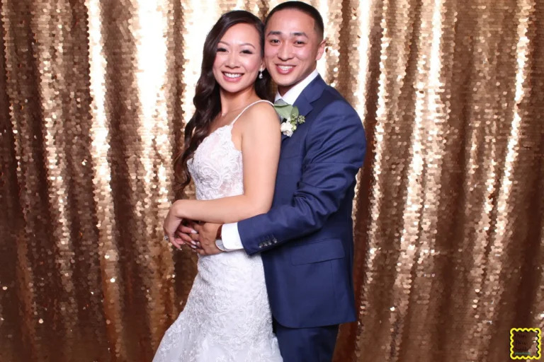 Wedding photo booth rental 1 Bride and groom embrace and smile in front of a gold sequin photo booth backdrop.
