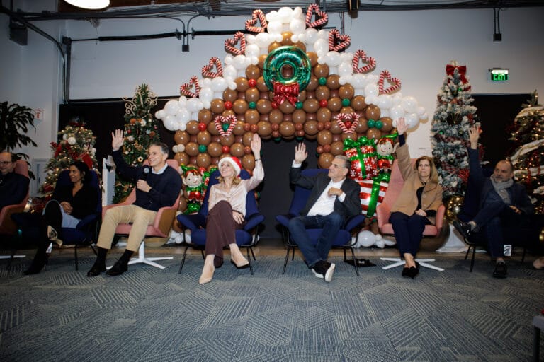 Panelists sit before a large holiday balloon arch while a speaker stands in the center.