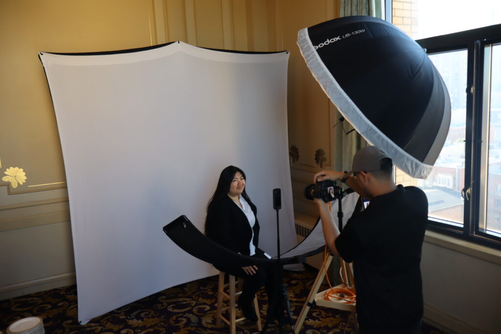 A professional attendee receiving an AI-enhanced LinkedIn headshot at a One, Two, Smile! Photobooth station.