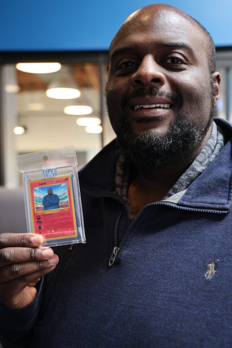 Smiling guest in a navy polo holds a personalized photo trading card beside their face.