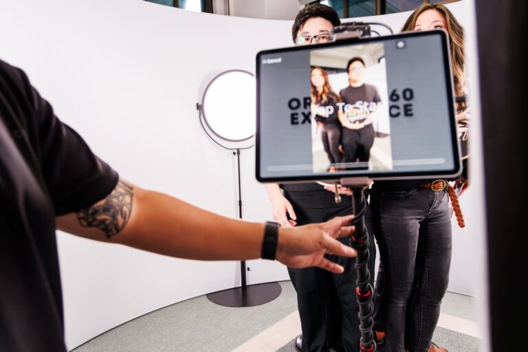 A tablet shows a preview of two guests posing on the video booth set.