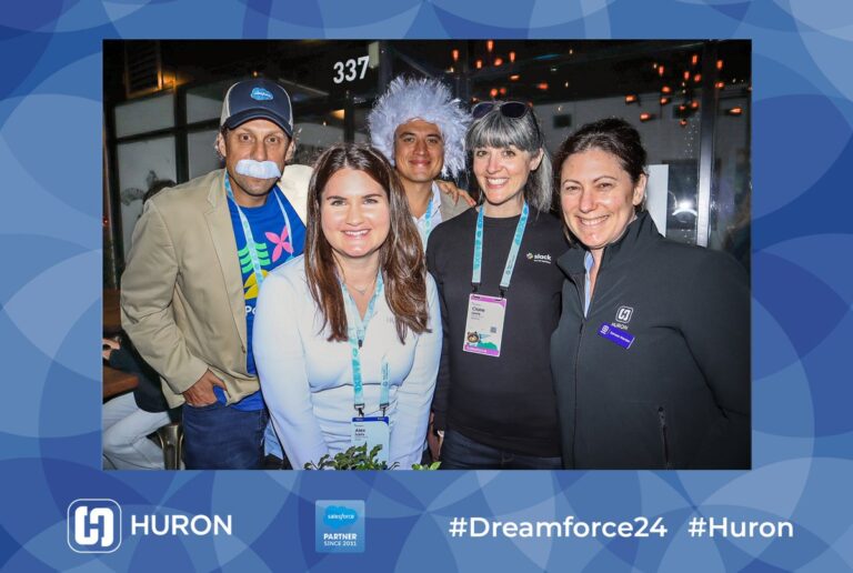 Guests wearing conference badges pose together in a blue branded photo frame.
