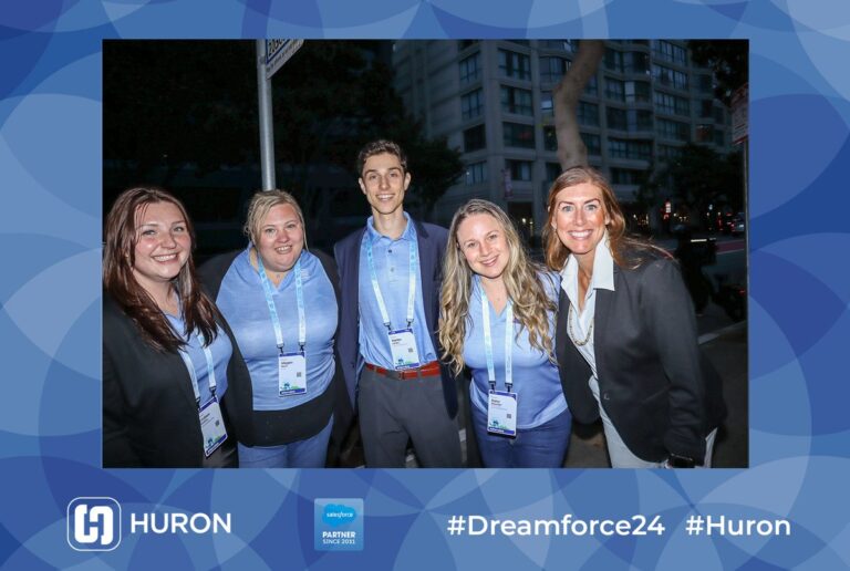 Five guests pose outdoors in a blue Huron-branded event photo frame.