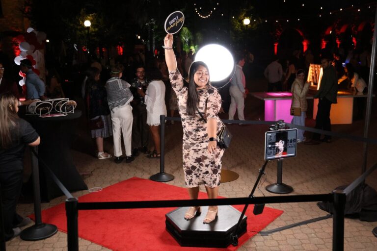Guest raises a prop beside a bright circular light on an evening 360 video set.