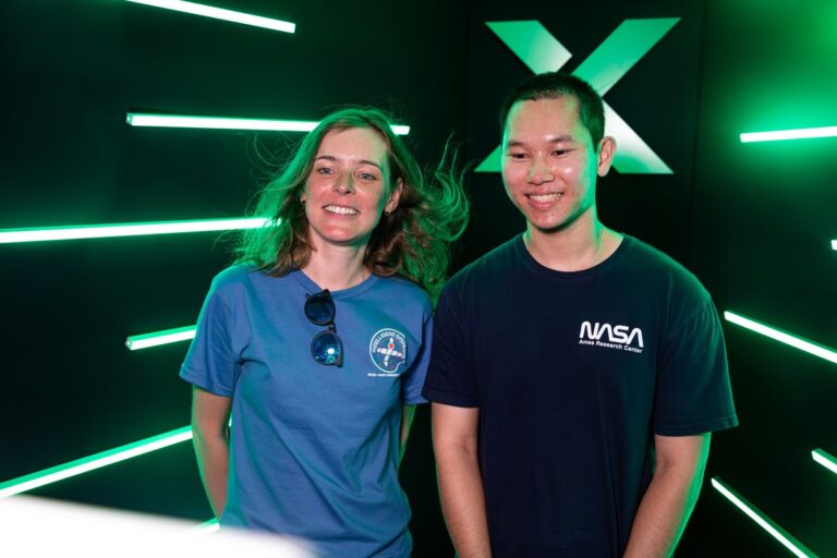 Two smiling guests in casual tops pose against the green LED backdrop.