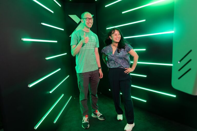 Two guests pose full length against green LED strips inside the booth.
