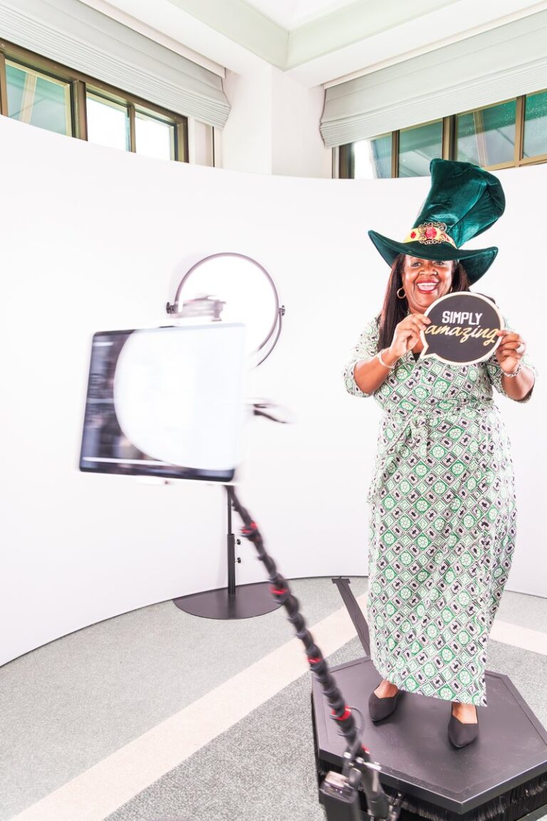 Guest in a patterned outfit poses with props beside the 360 camera arm.