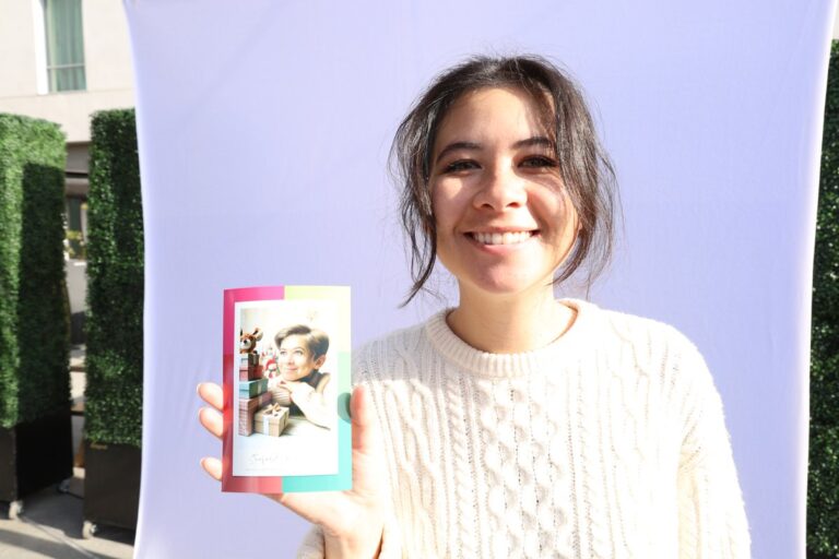 Chicago Photo Booth Rental 1 Guest in a white top holds a colorful portrait print beside a pale backdrop.