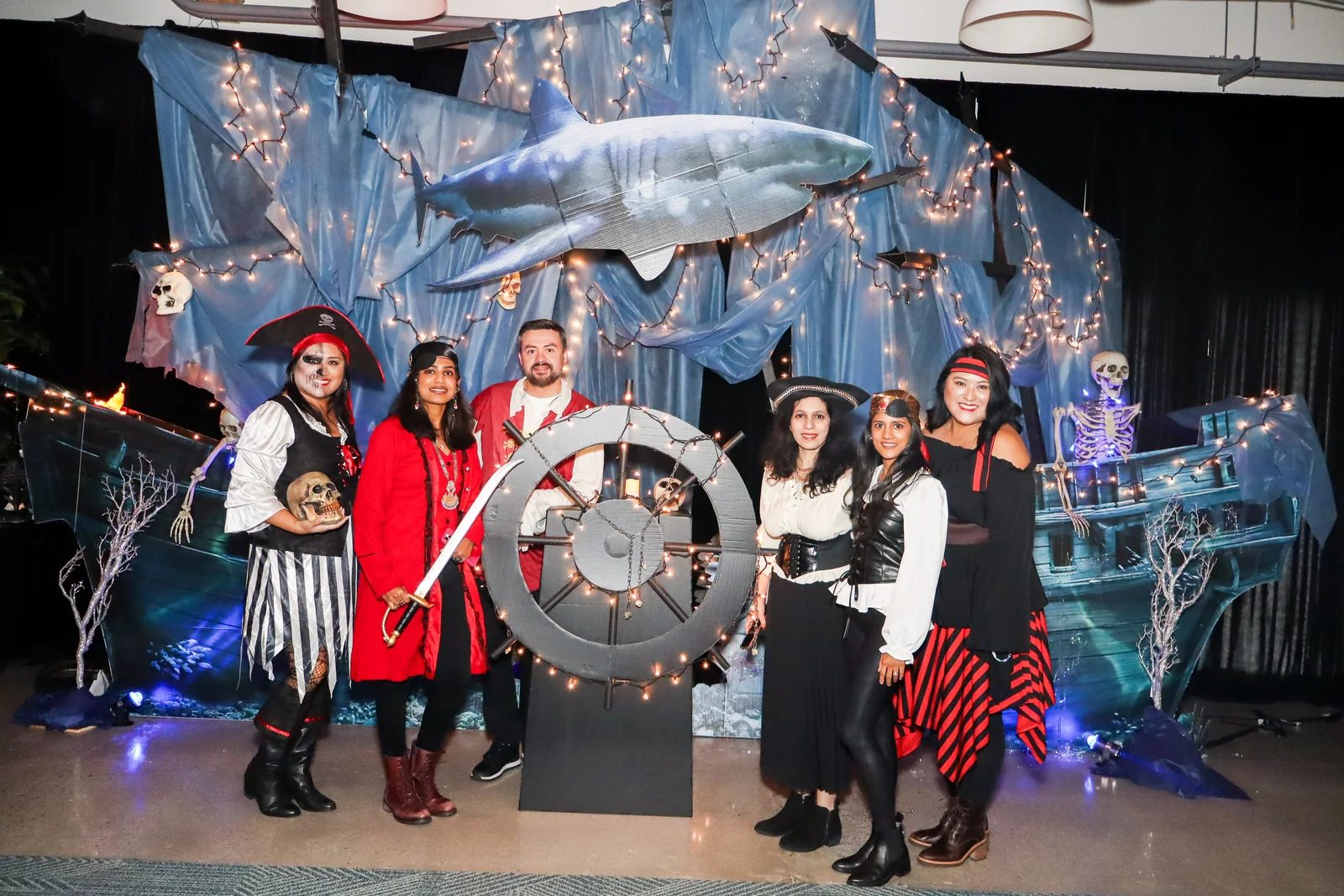 Costumed guests pose around a ship wheel in front of a pirate-themed Halloween backdrop.