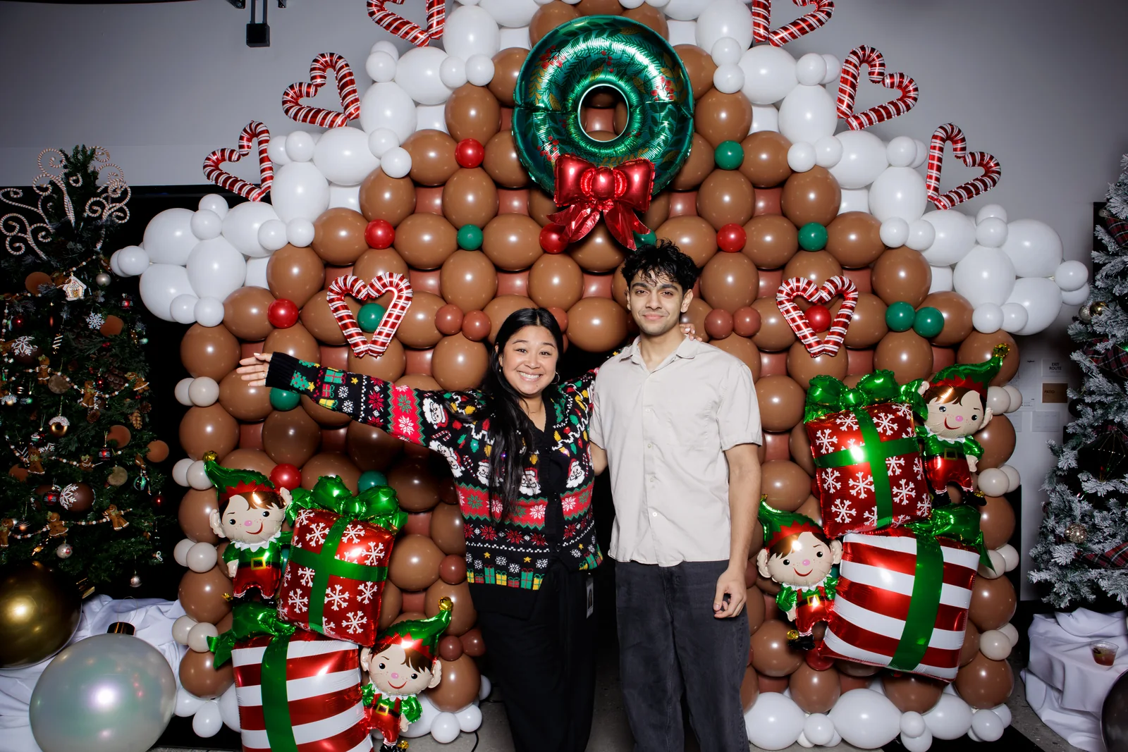 Three guests pose in front of a holiday balloon backdrop with candy-cane and gift decorations.