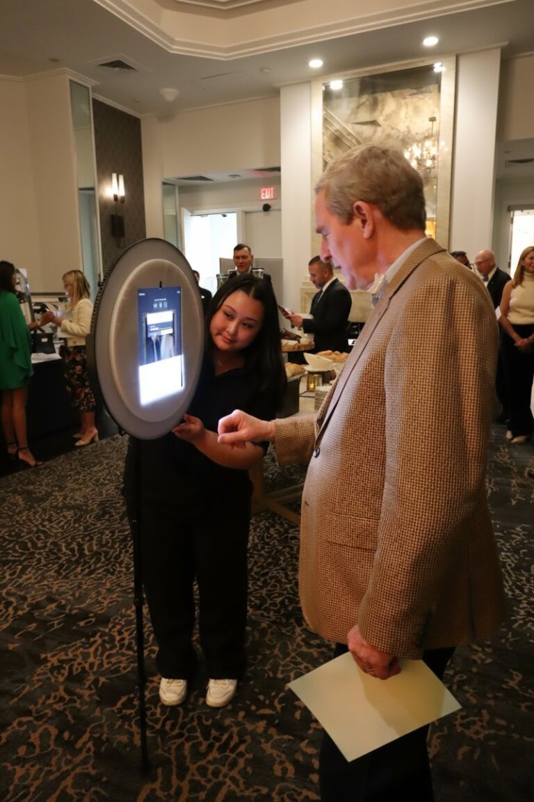 Attendant holds a portable photo booth toward a guest in a reception room.