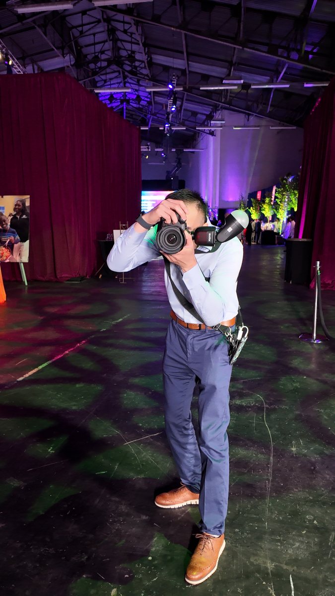 Photographer holds a camera at eye level in a purple-lit event hall.