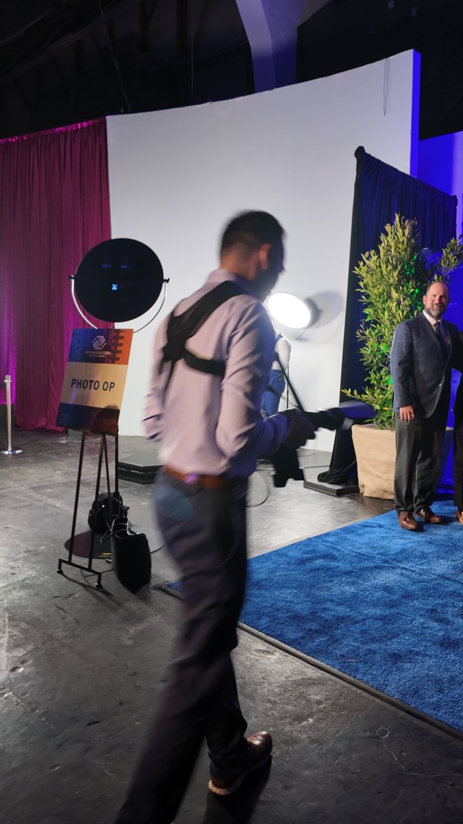 Miami Photo Booth Rental 4 Photographer carries a camera and lighting equipment across an event floor.