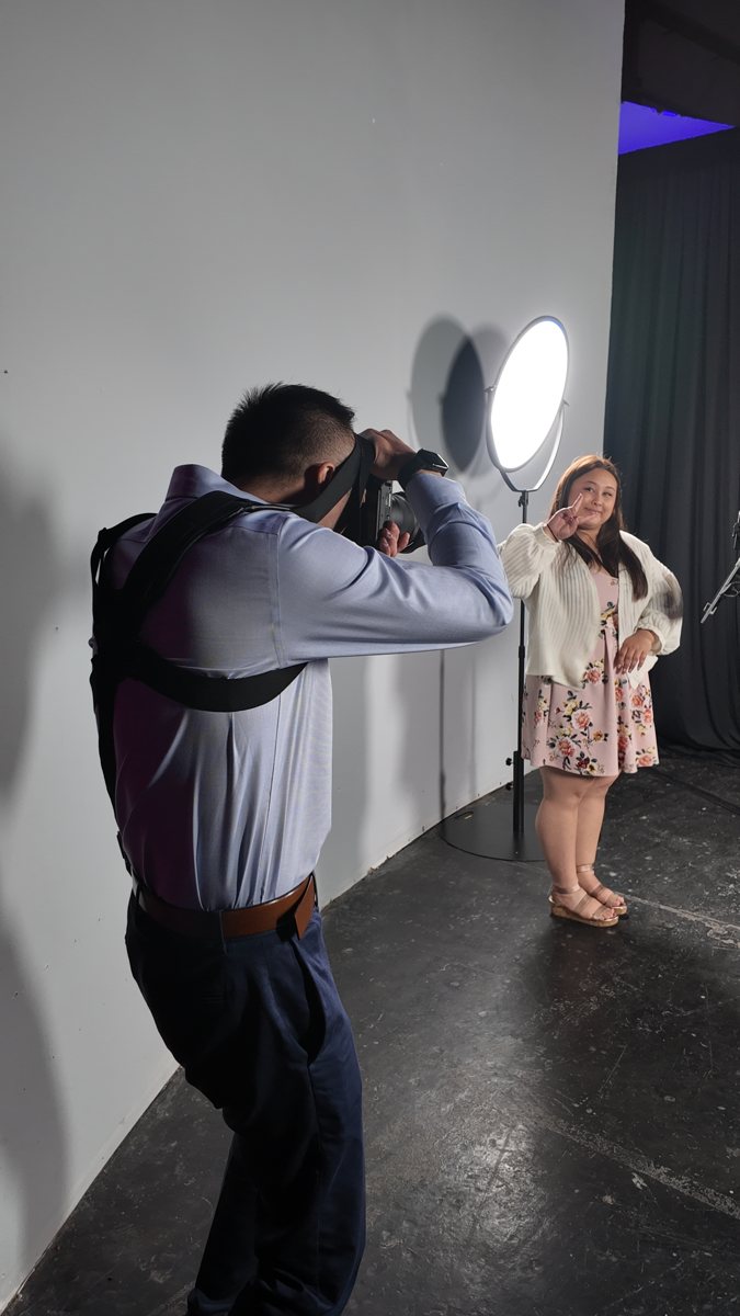 Photographer uses a camera and flash to photograph a guest beside a pale wall.